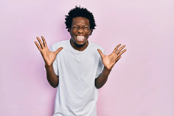 若いアフリカ系アメリカ人の男性は 腕を上げて興奮して叫んで目を閉じて成功のために狂気と狂気を祝うカジュアルな白いTシャツを着ている 勝者のコンセプト — ストック写真