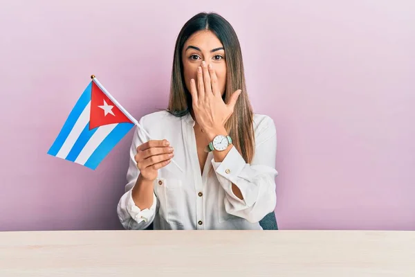 Młoda Latynoska Kobieta Trzymająca Flagę Kubańską Stole Zakrywająca Usta Dłonią — Zdjęcie stockowe