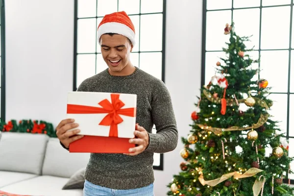 Young Hispanic Man Unpacking Gift Standing Christmas Tree Home — Stok fotoğraf