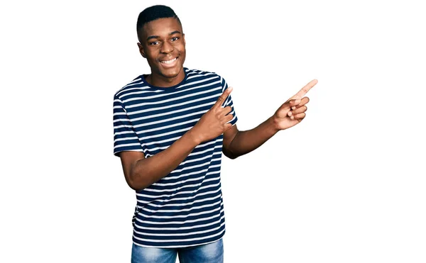 カジュアルなストライプのTシャツを着た若いアフリカ系アメリカ人の男性が笑顔でカメラを見て 両手と指を横に向けて — ストック写真
