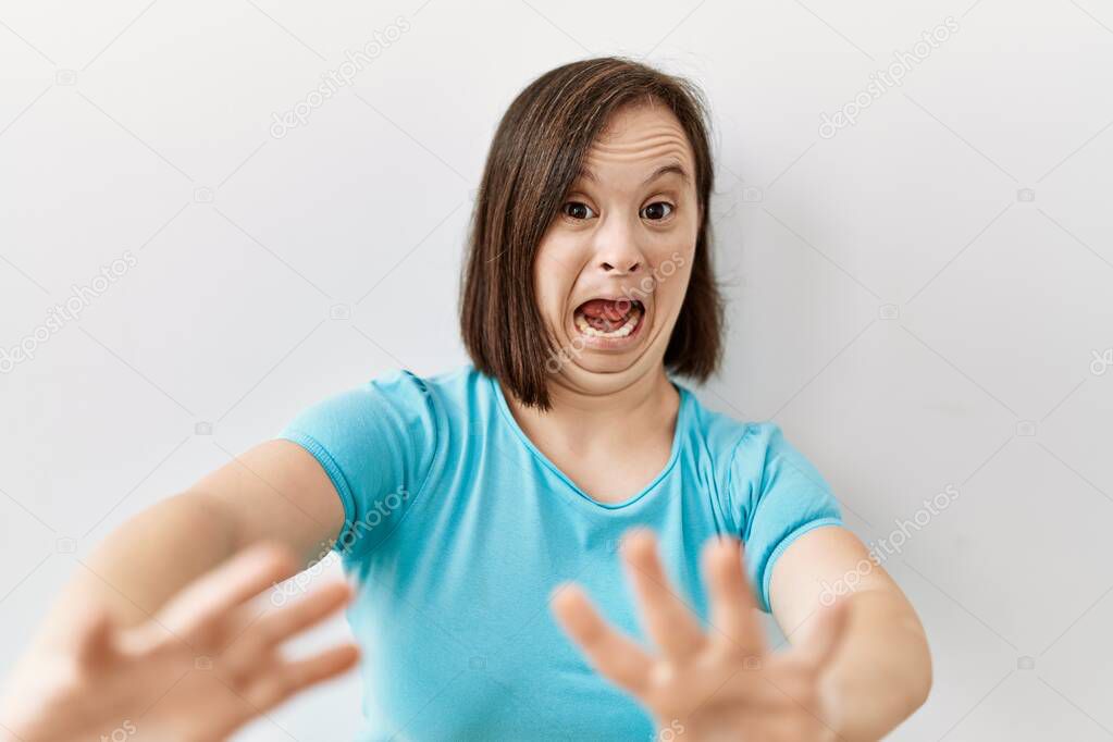 Young down syndrome woman standing over isolated background afraid and terrified with fear expression stop gesture with hands, shouting in shock. panic concept. 