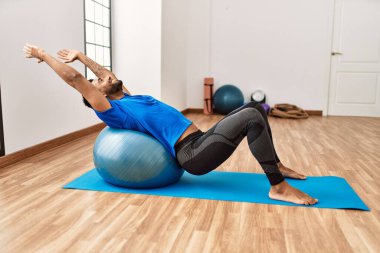 Yakışıklı İspanyol adam egzersiz yapıyor ve yoga minderinde geriniyor, spor salonunda pilates topuyla esneklik gösteriyor.