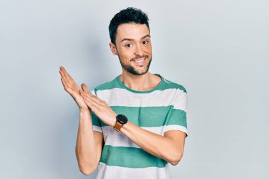 Latin asıllı genç adam, günlük kıyafetler giyip alkışlıyor ve mutlu, neşeli ve gururlu elleri bir arada alkışlıyor. 