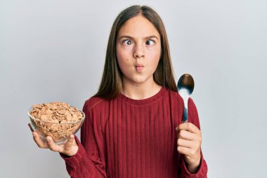 Güzel esmer küçük kız sağlıklı tahıl gevrekleri yiyor. Kaşıkla balık yüzü yapıyor. Ağızlarıyla ve şaşı gözleriyle, çılgın ve komik.. 