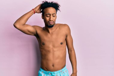 Young african american man with beard wearing swimsuit confuse and wonder about question. uncertain with doubt, thinking with hand on head. pensive concept. 