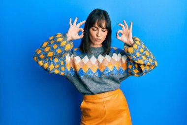 Günlük kazak giyen genç İspanyol kadın rahatla ve gülümse gözleri kapalı parmaklarıyla meditasyon hareketi yapıyor. yoga konsepti. 