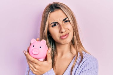 Güzel İspanyol kadının elinde domuz kumbarası ve kafası karışık bir ifade var. şüphe kavramı. 