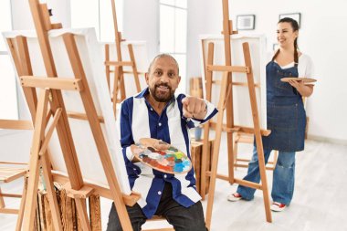 Senior artist man at art studio pointing to you and the camera with fingers, smiling positive and cheerful 