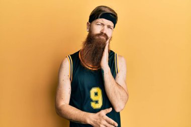 Uzun sakallı, basketbol forması giyen kızıl saçlı adam kollarını kavuşturarak depresyondan sıkılmış ve yorgun göründüğünü düşünüyor.. 