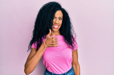 Orta yaşlı Afro-Amerikalı kadın günlük giysiler giyip mutlu bir el hareketi yapıyor. Kameraya bakıp başarıyı gösteren ifade. 