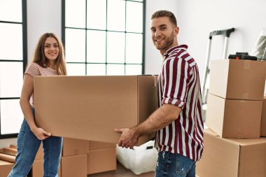 Genç beyaz çift mutlu bir şekilde gülümsüyor. Yeni evlerinde karton kutu tutuyorlar..