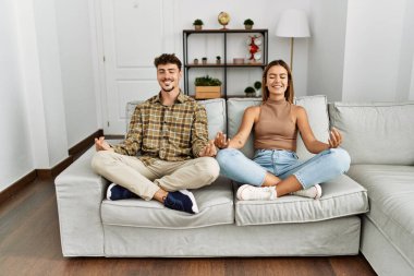 Mutlu köpek yoga egzersizi gülümseyen İspanyol çift evdeki kanepede oturuyor..