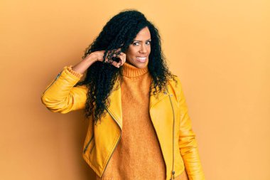 Orta yaşlı Afro-Amerikalı kadın yün kazak ve deri ceket giyip tek parmağıyla kafasını gösteren gülümseme, harika bir fikir ya da düşünce, iyi bir hafıza. 