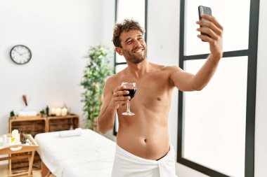 Şarap içen genç İspanyol adam güzellik merkezindeki akıllı telefondan selfie çekiyor.