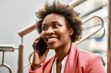 Güzel iş kadını afro saçlı Afro-Amerikan kadın mutlu ve kendinden emin bir şekilde şehirde telefonda konuşuyor.