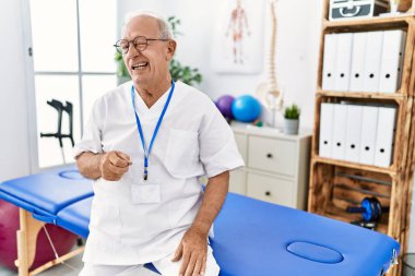 Senior physiotherapy man working at pain recovery clinic winking looking at the camera with sexy expression, cheerful and happy face. 