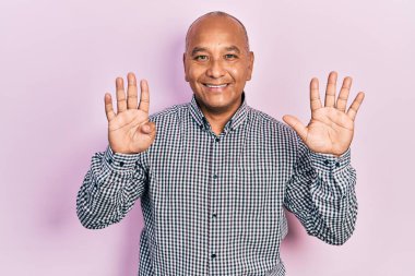 Orta yaşlı, gündelik kıyafetler giyen Latin bir adam dokuz numarayı gösterip işaret ederken kendinden emin ve mutlu bir şekilde gülümsüyor.. 