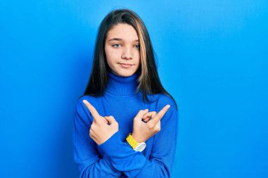 Young brunette girl wearing turtleneck sweater pointing to both sides with fingers, different direction disagree 