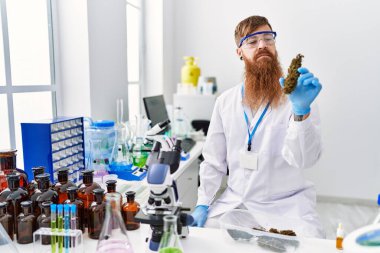 Laboratuvarda marihuana otu taşıyan bilim adamı üniforması giyen genç bir kızıl.