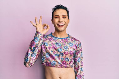 Handsome man wearing make up wearing fashion clothes smiling positive doing ok sign with hand and fingers. successful expression. 