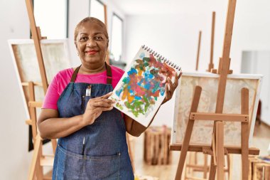 Kıdemli Afro-Amerikan kadın gülümsüyor sanat stüdyosunda kendine güvenen çizim defteri tutuyor.