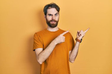 Sakallı, sıradan, sarı tişörtlü beyaz bir adam iki eli de endişeli ve gergin, endişeli ve şaşırmış bir ifade sergiliyor. 