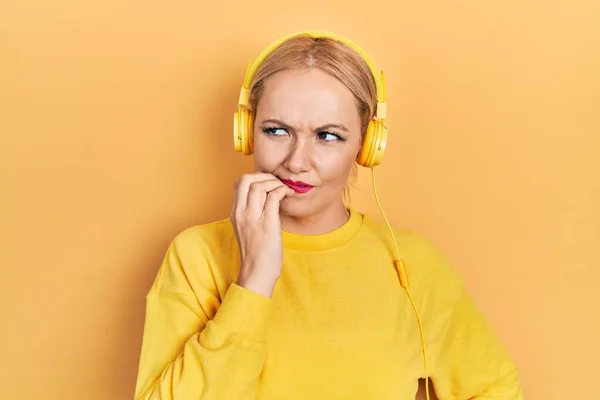 若いブロンドの女性は 口の爪をかむ上で手でストレスと緊張を見てヘッドフォンを使用して音楽を聴いています 不安の問題 — ストック写真