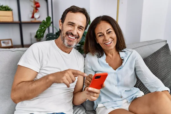 中年男性と女性カップル使用スマートフォン座って上のソファに家 — ストック写真