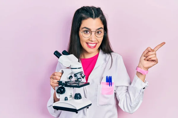 Молода Дівчина Уніформі Вченого Тримає Мікроскоп Усміхнений Щасливий Вказуючи Рукою — стокове фото