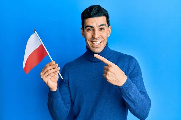 英俊的惊慌失措的男人举着波兰国旗 高兴地微笑着 手指手画脚 — 图库照片