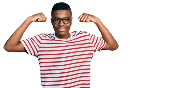 年轻的非洲裔美国人 身穿休闲装 戴着眼镜 露出胳膊肌肉 带着自豪的笑容 健身概念 — 图库照片
