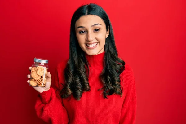 Young Hispanic Woman Holding Salty Biscuits Jar Looking Positive Happy — Stock fotografie