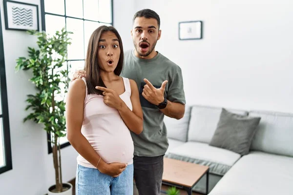 Young Interracial Couple Expecting Baby Touching Pregnant Belly Surprised Pointing — Stock Photo, Image