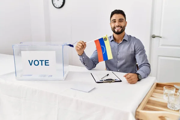 政治選挙で髭を生やした若いハンサムな男がベネズエラの旗を持っています肯定的で幸せな立っていると歯を示す自信を持って笑顔で笑顔 — ストック写真