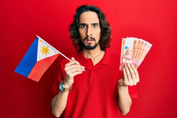 Young Hispanic Man Holding Philippines Flag Pesos Banknotes Clueless Confused — Stock Photo, Image