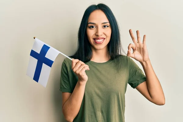 Young Hispanic Girl Holding Finland Flag Doing Sign Fingers Smiling — 스톡 사진