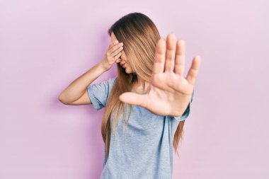 Sıradan tişörtler giyen, elleriyle gözlerini kapatan, üzgün ve korku dolu hareketler yapan genç sarışın kız. utangaç ve olumsuz kavram. 