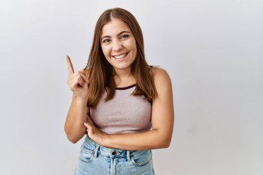 Genç esmer kadın izole edilmiş arka planda duruyor, yüzünde kocaman bir gülümsemeyle, eli ve parmağı kameraya bakıyor.. 