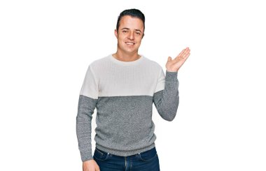 Yakışıklı, kışlık süveter giyen neşeli bir şekilde gülümseyen ve avuç içi kameraya bakan genç bir adam.. 