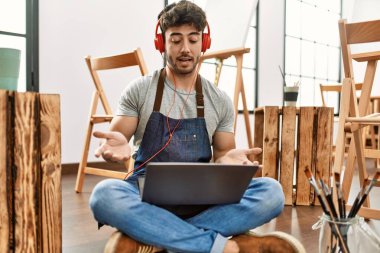 Genç İspanyol ressam, sanat stüdyosunda kulaklık ve dizüstü bilgisayar kullanarak video görüşmesi yapıyor..