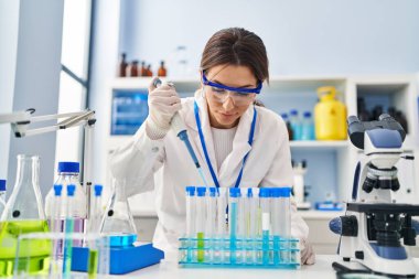 Laboratuvarda pipet kullanan, bilim adamı üniforması giyen İspanyol genç bir kadın.