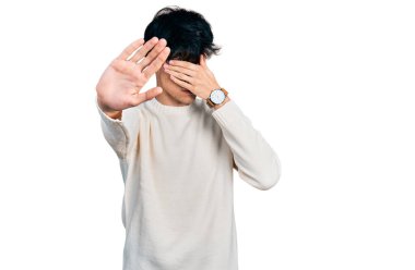 Yakışıklı hippi genç adam gündelik bir kazak giyiyor elleriyle gözlerini kapatıyor ve üzgün ve korku ifadeleriyle jest yapıyor. utangaç ve olumsuz kavram. 