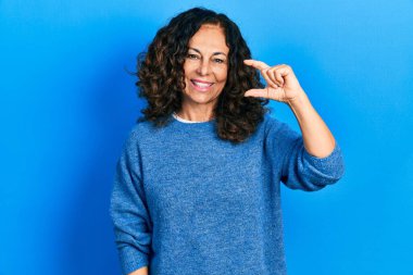 Orta yaşlı İspanyol kadın günlük kıyafetler giyiyor gülümsüyor ve el hareketleriyle küçük boy işaretler yapıyor parmaklarıyla ve kamerayla bakıyor. ölçüm kavramı. 