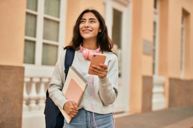 Genç ortadoğulu kız şehirde akıllı telefon kullanarak mutlu bir şekilde gülümsüyor..