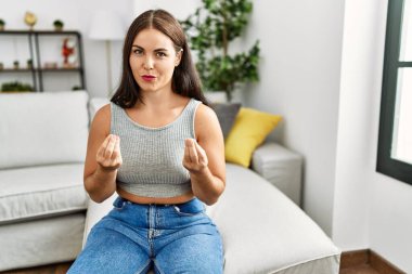 Genç esmer kadın evdeki kanepede oturuyor. Elleriyle para hareketi yapıyor. Maaş istiyor. 