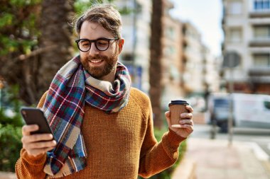 Güneşli bir günde akıllı telefon kullanan sakallı beyaz bir genç adam.