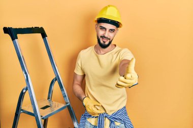 İnşaat merdivenlerinde sakallı yakışıklı, kasketli, neşeli gülümsemeli, yardım eli uzatan ve kabul gören bir adam.. 