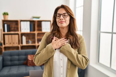 Danışma ofisinde çalışan İspanyol kadın elleri göğsünde, gözleri kapalı, yüzünde minnet dolu bir jestle gülümsüyor. sağlık kavramı. 