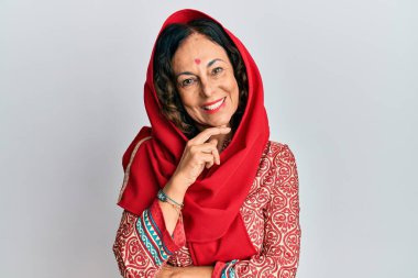 Orta yaşlı İspanyol kadın geleneksel Sherwani sari giysileri giyiyor kameraya kendinden emin bakıyor kollarını kavuşturmuş ve çenesini kaldırmış gülümsüyor. Olumlu düşünmek. 