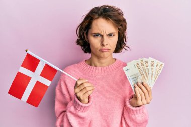 Elinde Norveç bayrağı ve Krone banknotları tutan esmer bir kadın sıkıntılı ve endişeli, sinirli ve korkmuş bir halde. hüzünlü ifade. 